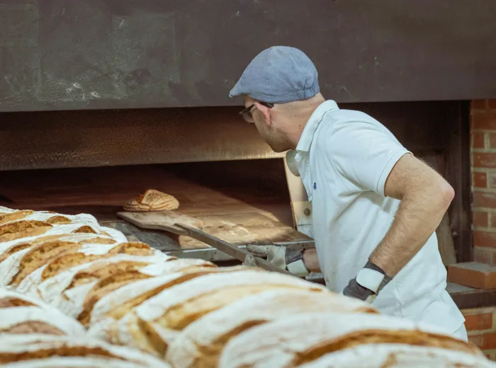 Boulanger artisan enfournant du pain à l'aide d'une pelle en bois dans un four traditionnel