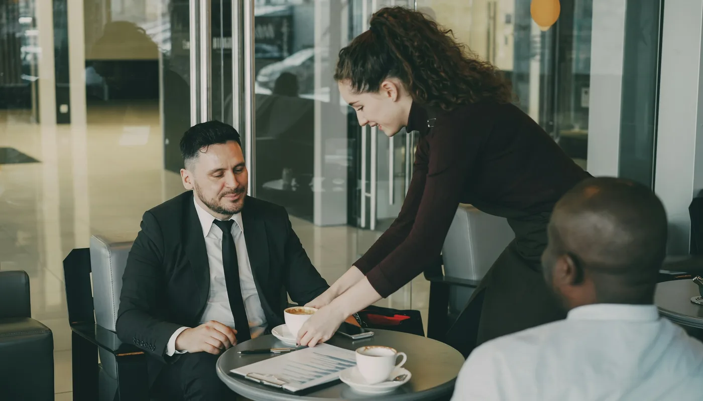 Serveuse apportant un café à deux clients attablés, moment de service attentionné dans un petit commerce