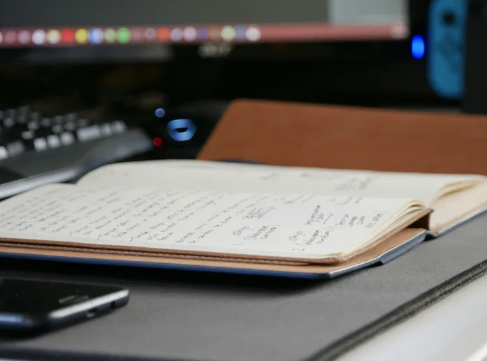 Carnet ouvert avec des notes manuscrites sur un bureau, à côté d'un clavier et d'un téléphone