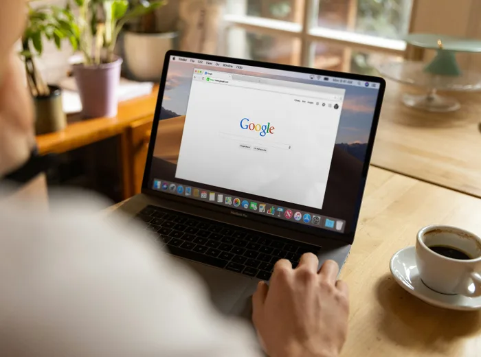 Personne assise devant un ordinateur portable ouvert sur la page de recherche Google, tasse de café à côté